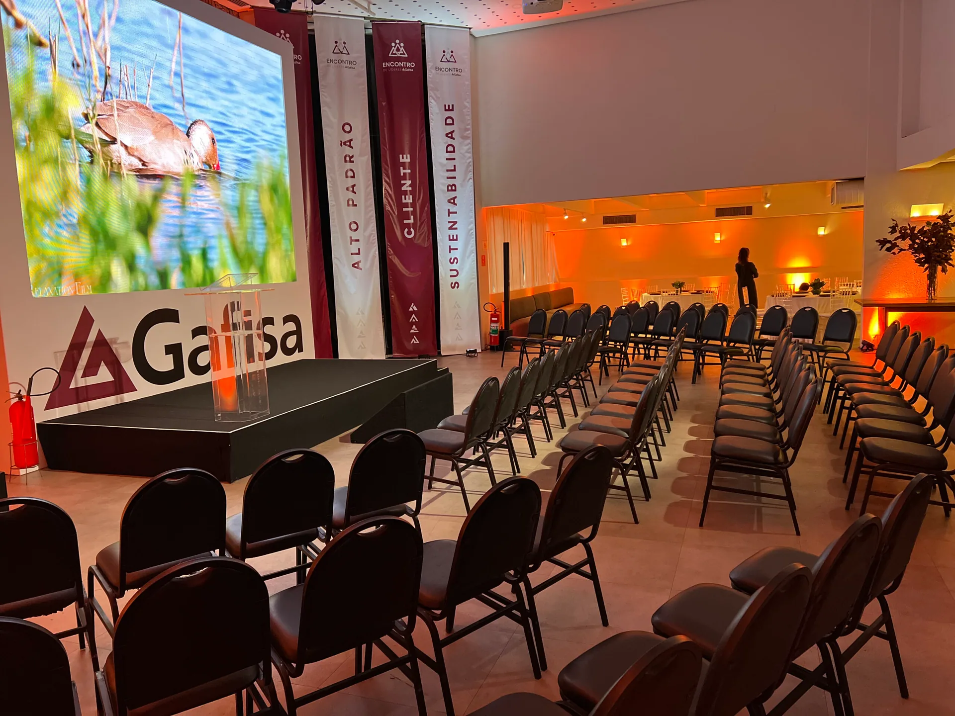 Auditório montado para evento de lançamento imobiliário, com telão e iluminação cênica