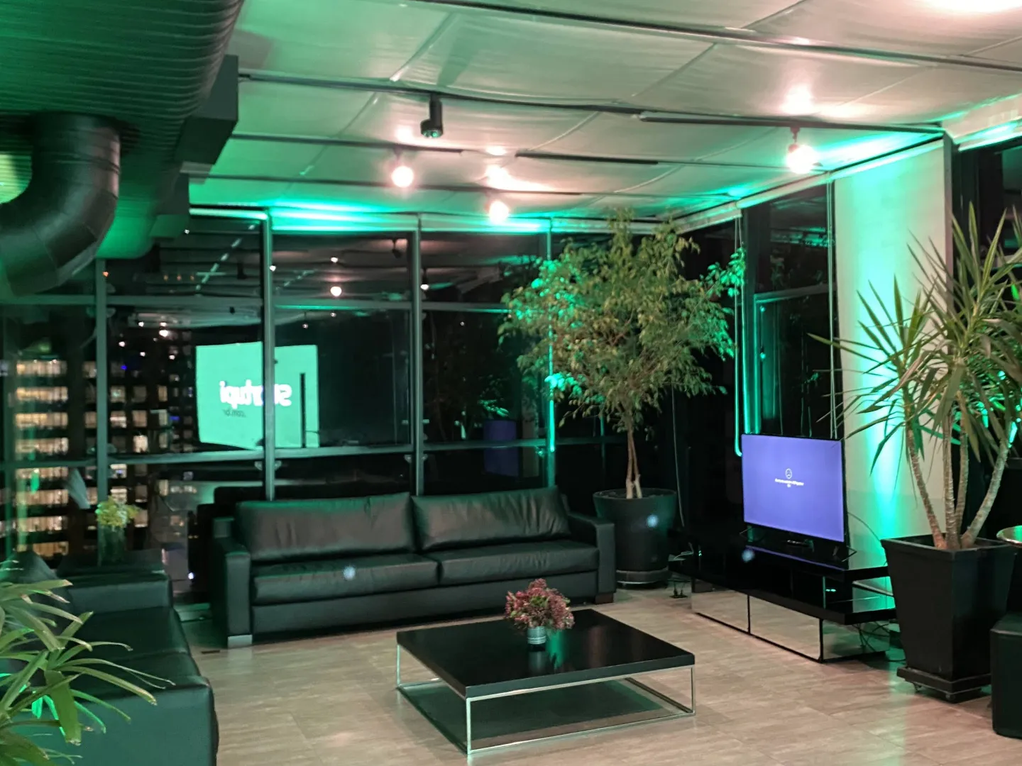 Lounge do rooftop com sofás, plantas e iluminação cênica