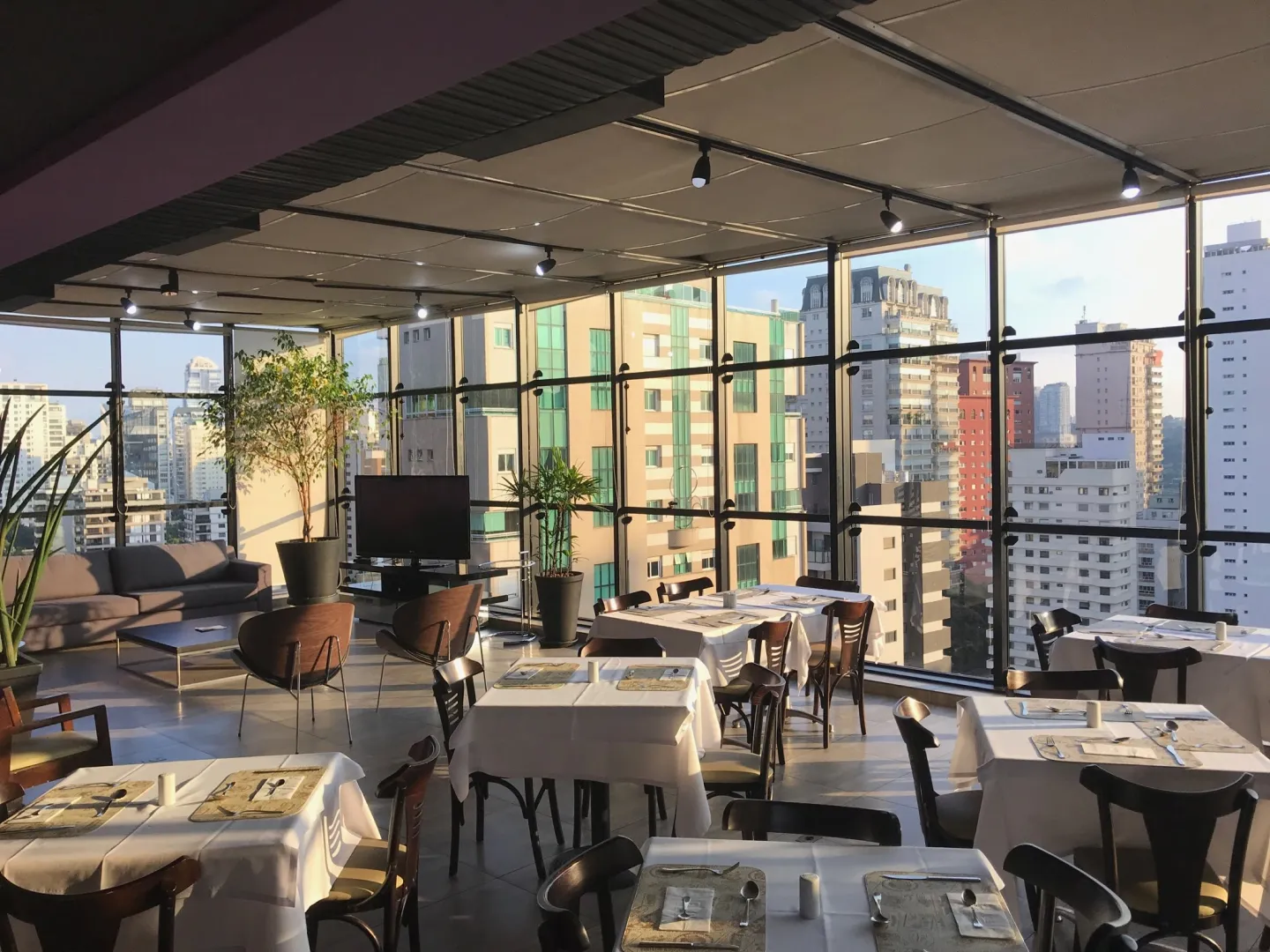 Rooftop envidraçado do piso ao teto com mesas postas e vista urbana